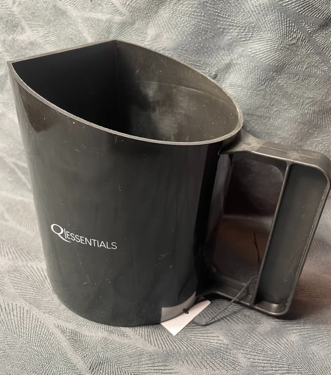 Sort plastik mælkeskummer med mærket "QI ESSENTIALS" på siden, placeret på en grå tekstureret overflade.