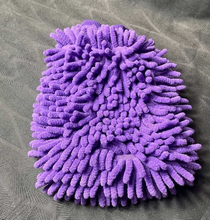 Lilla mikrofiber vaskehandske med fyldige, bløde nupper lagt på en grå overflade.