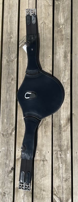Sort læder gjord med metal spænder og D-ring, lagt på træplanker.