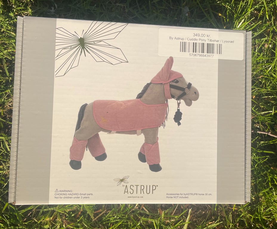 Billede af en æske med tilbehør til byASTRUP Cuddle Pony, inklusive lyserøde dækkener og beskyttelse til ponyens ben og hoved, prissat til 349,00 kr.