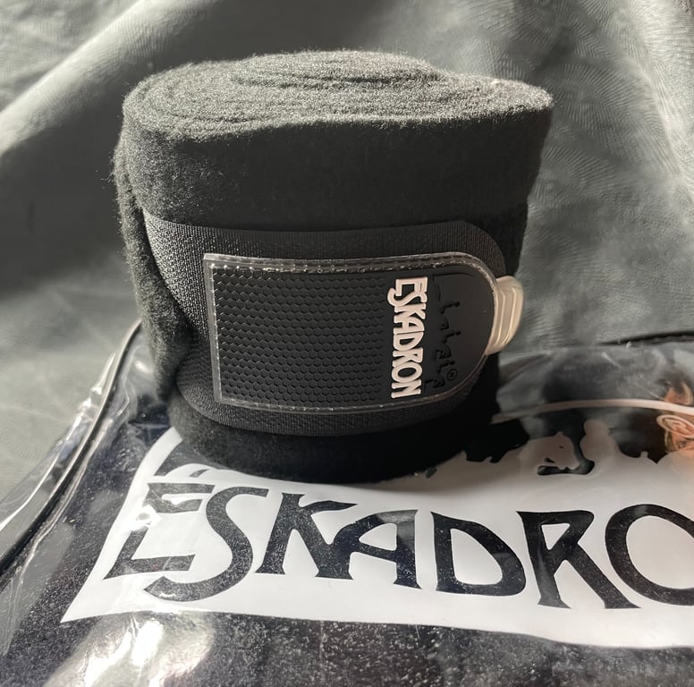Sort fleecemateriale Eskadron bandage til hest med logo, placeret på en Eskadron plastikpose med logo.