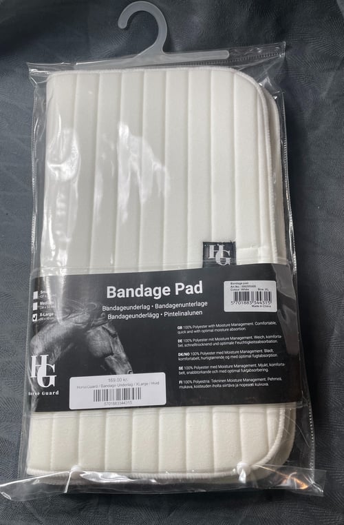Bandageunderlag i hvidt, quiltet materiale, pakket i gennemsigtig plast med etikette. (1)