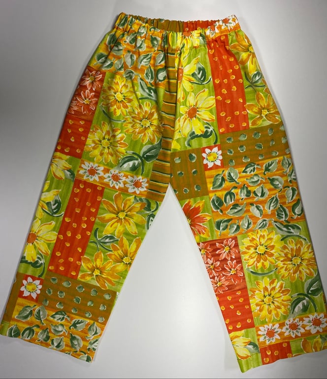 Bukser med elastik i taljen og et patchwork-mønster bestående af gule, orange og grønne felter med blomster og blade.