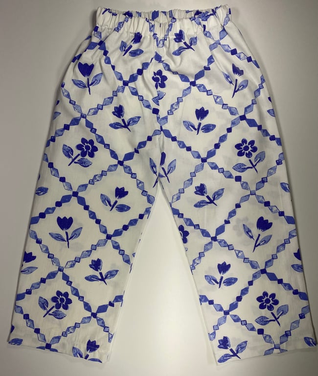 Billede af et par bukser i hvid med mønster af blå blomster og diagonale tern. Bukserne har elastik ved taljen.