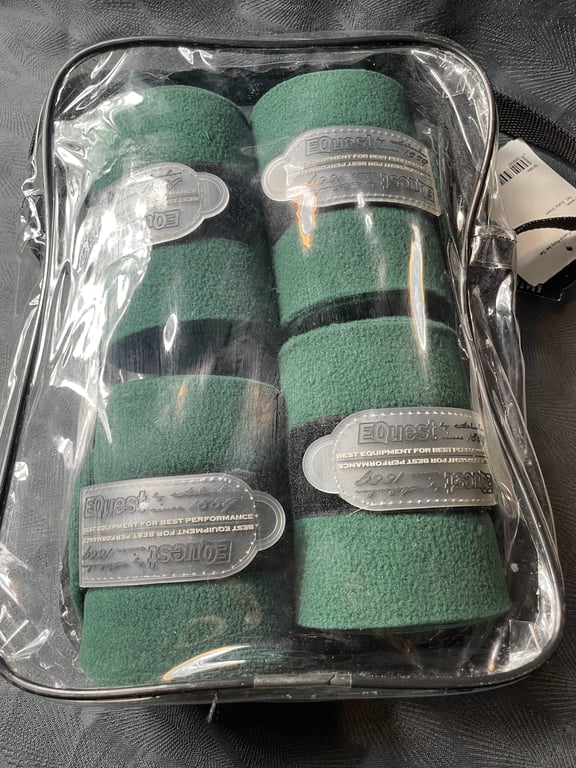 Gennemsigtig plastikpose indeholdende fire grønne fleecebandager med sorte velcroremme og sølvfarvede mærkater, placeret på en mørk overflade.