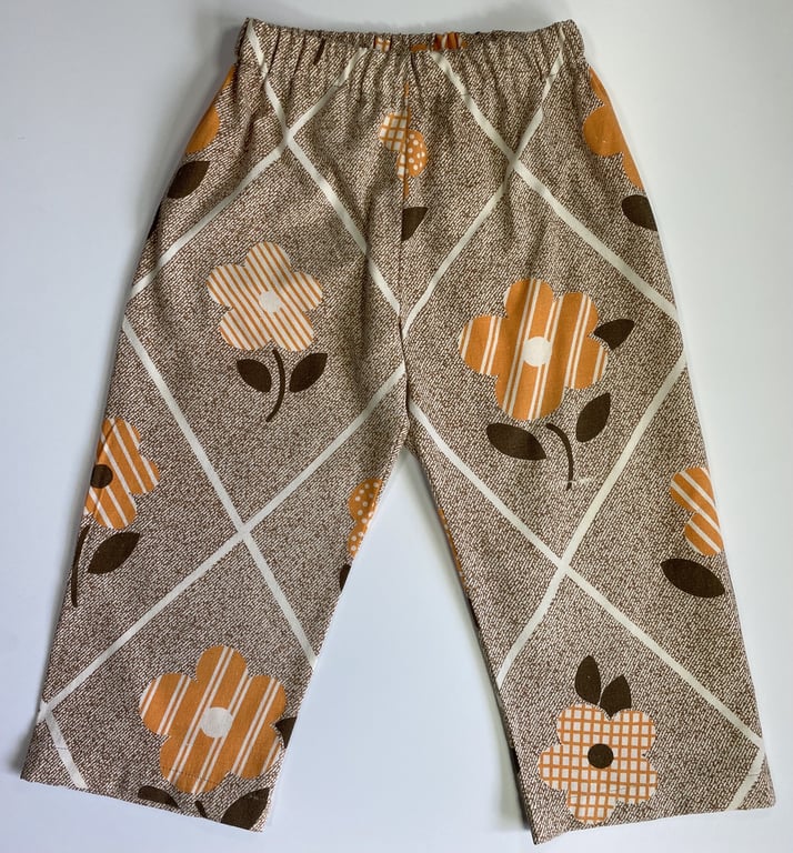 Bukser med elastik i taljen, beige-beige mønster med orange, hvide og brune blomster samt diagonale hvide linjer.