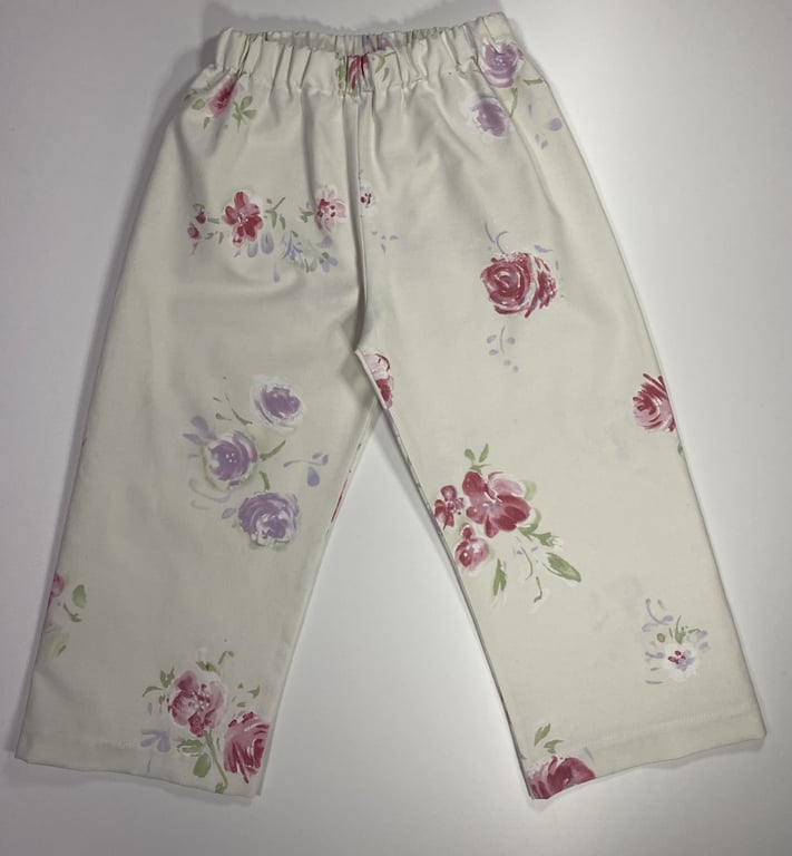 Bukser til børn med elastik i taljen, cremefarvede med blomsterprint i lyserød, lilla og grøn.