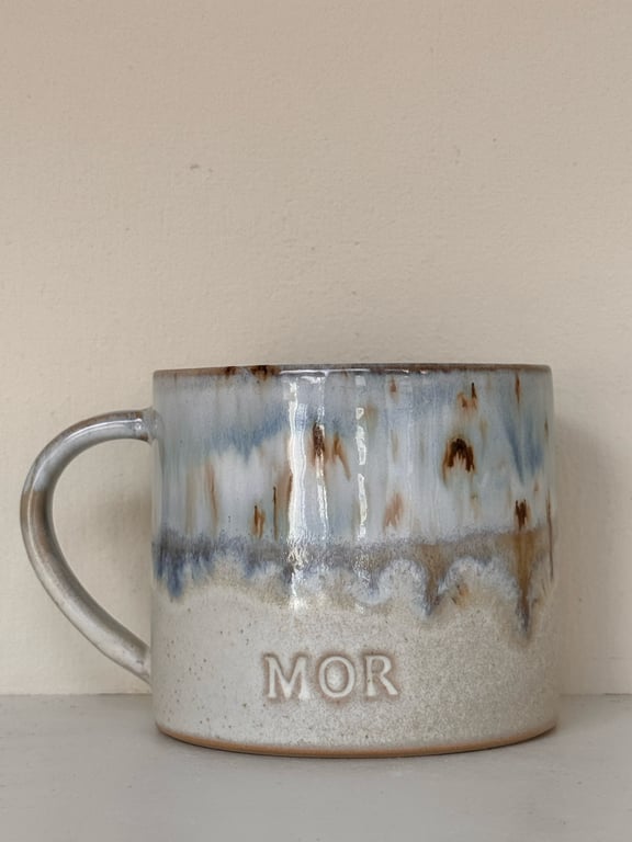 Keramikkrus med blå, brune og hvide glasurer, med teksten "MOR" præget på forsiden.