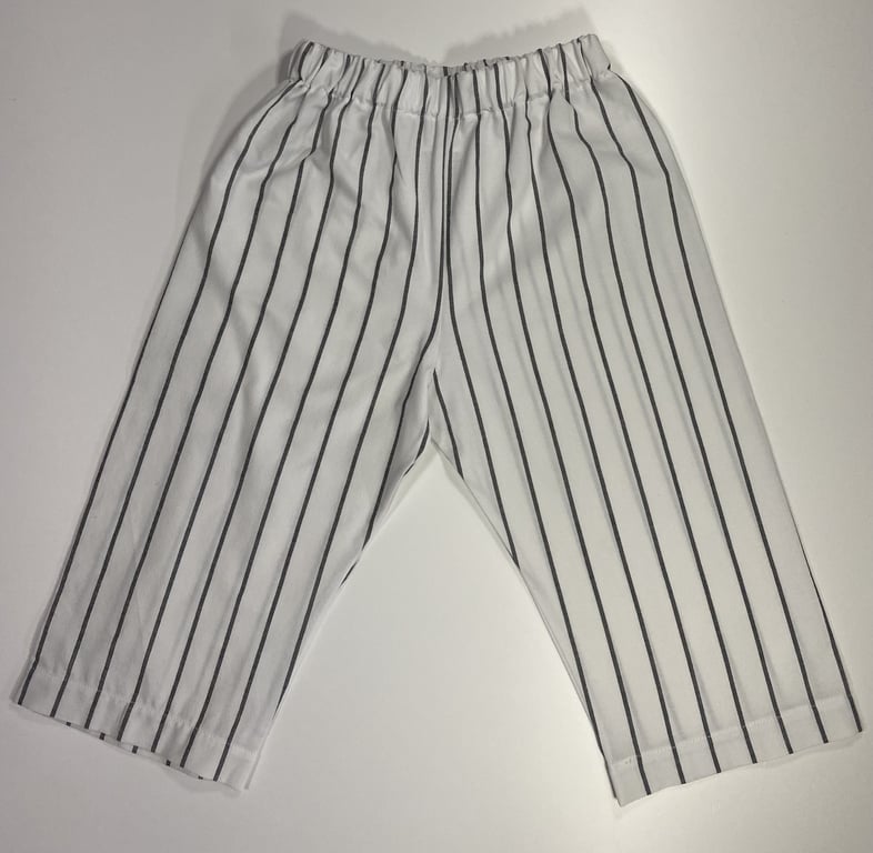 Billede af hvidt par bukser med sorte lodrette striber og elastisk talje, lagt fladt på hvid baggrund.
