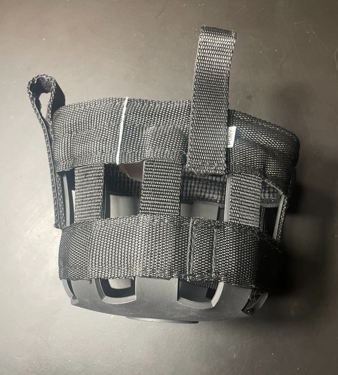 Sort hundemuzzle lavet af nylonremme og plast, set ovenfra på en mørk overflade.