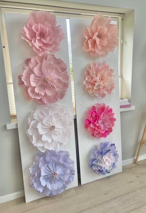 To store paneler med store, håndlavede papirblomster i forskellige rosa, hvide, pink og lilla nuancer, placeret mod et vindue i et lyst rum. (1)