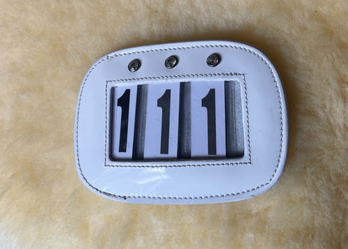 Hvid stykke læder eller plastik med tre hæfteknapper øverst og et vindue, der viser tre-cifret tal "111". (1)