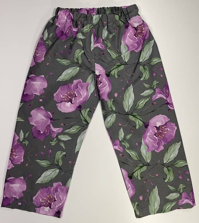 Billede af grå bukser med elastik i taljen og mønster af store lilla blomster med grønne blade.