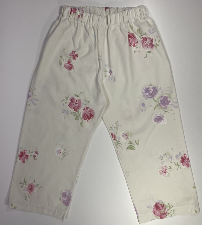 Bukser til børn med elastisk talje, cremefarvet med blomstermønster i pink, lilla og grøn.