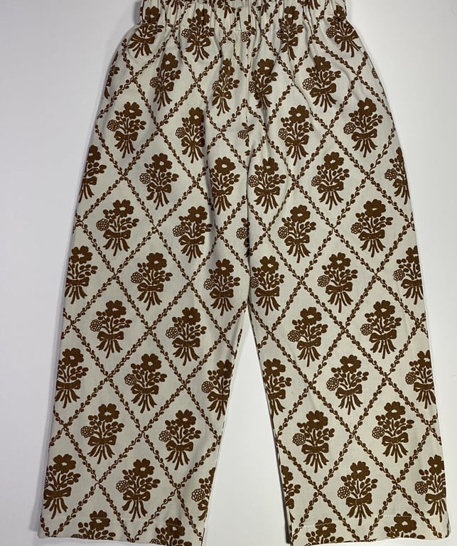 Bukser med elastisk talje, i hvidt stof med brun blomstermønster arrangeret i diamantformede felter.