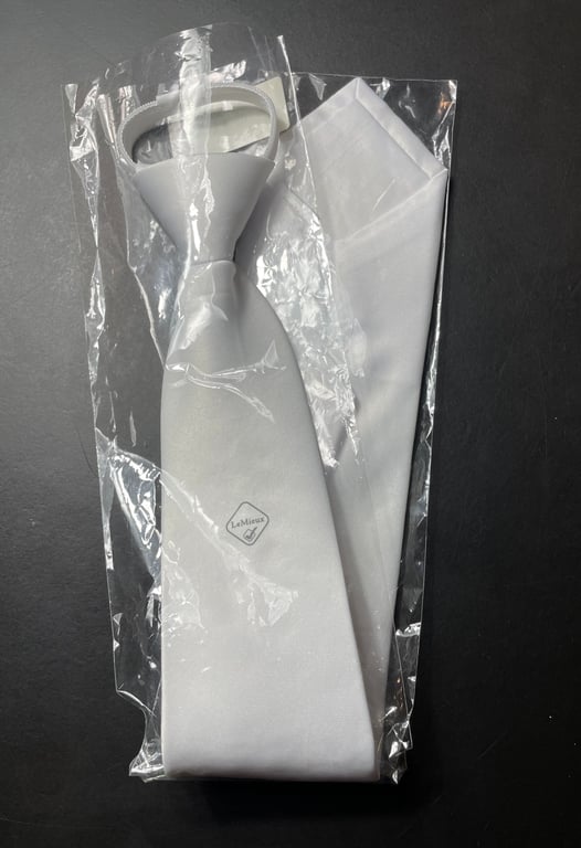 Hvid slips og lommetørklæde i plastikpose på sort baggrund.