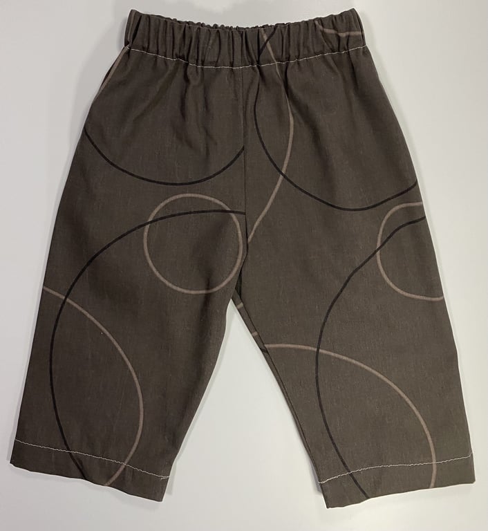 Brune babybukser med elastisk talje og abstrakte, buede linjer i sort og beige.