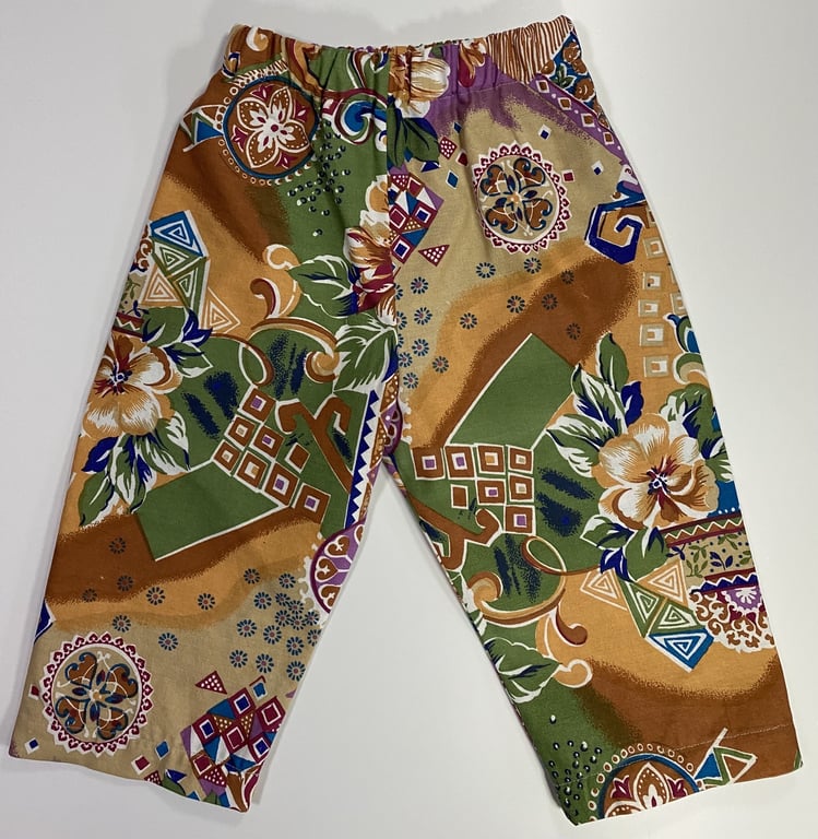 Billede af bukser med elastisk talje med farverigt, abstrakt mønster bestående af blomster, geometriske former og dekorative elementer i nuancer af grøn, lilla, brun, beige og blå.
