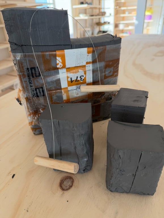 En blok plastilin ler og flere mindre klumper, med to trådskærere med træhåndtag placeret foran leret på et lyst træbord.