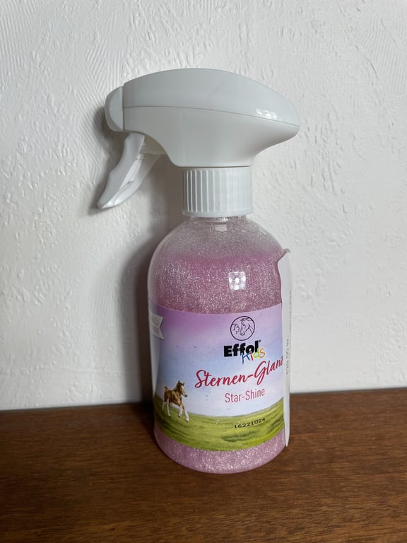 Flaske med sprøjtemekanisme indeholdende Effol Kids Sternen-Glanz (Star-Shine), en pink glitrende væske, står på en træoverflade mod en hvid væg.