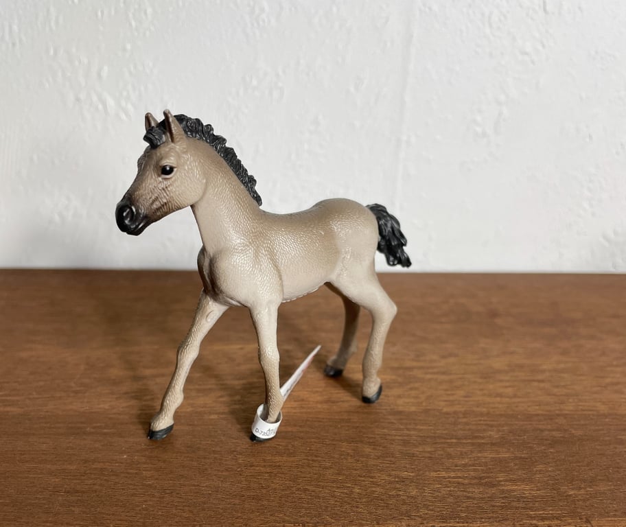 Model af en brun hest med sort man og hale, stående på et brunt bord mod en hvid væg.