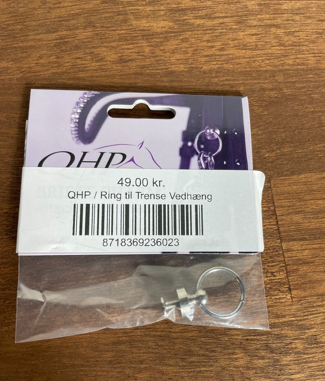 Pakke med en metalring til trense vedhæng fra mærket QHP, pris 49,00 kr., lagt på en træbordplade.