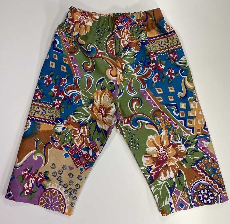 Buks i stoffet med elastisk talje og farverigt mønster bestående af blomster og geometriske former i grøn, blå, lilla, brun og beige.