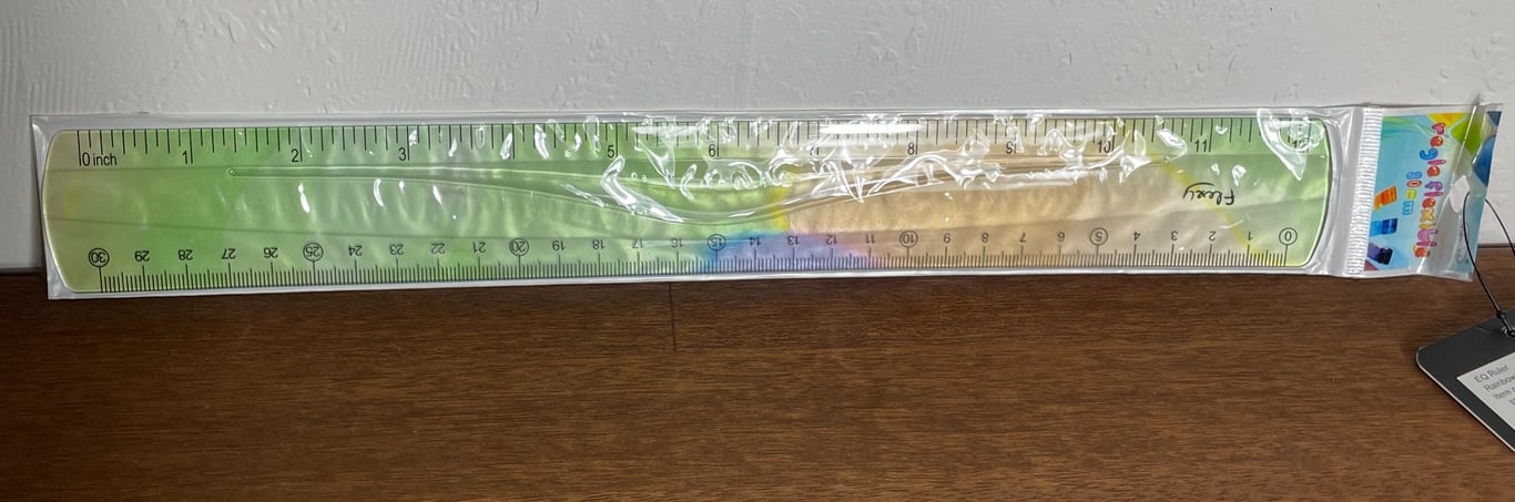 Lineal med dobbeltsidet måleskala i centimeter og tommer, med regnbuefarvet og grøn baggrund, pakket i gennemsigtigt plast.