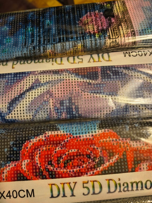 Nærbillede af flere indpakkede DIY 5D diamantmalerier med alfanumeriske symboler til vejledning.