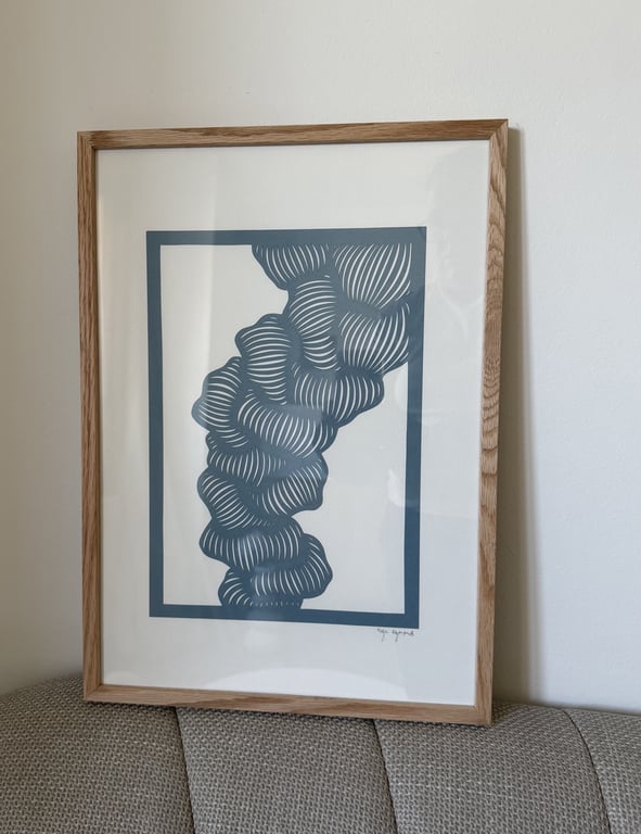 Indrammet abstrakt kunst med blå, buede linjer og former på hvid baggrund, placeret på en grå sofa mod en hvid væg.