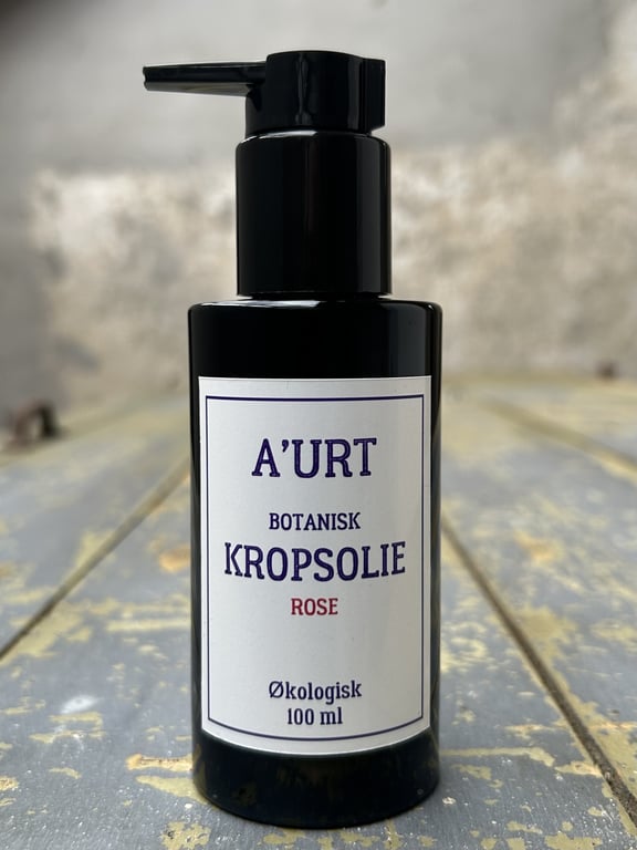 Sort pumpeflaske med label, der viser A'URT botanisk kropsolie med rose duft, 100 ml økologisk.