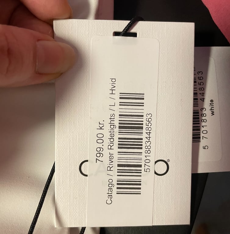 Et billede af et prisetiket med teksten "799,00 kr. Catago / River Ridetights / L / Hvid" og en stregkode, holdt af en hånd.