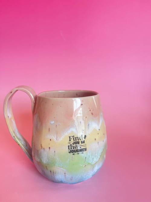 Keramisk krus med farverige pastelfarver og teksten "Find joy in the journey" mod en lyserød baggrund. (1)