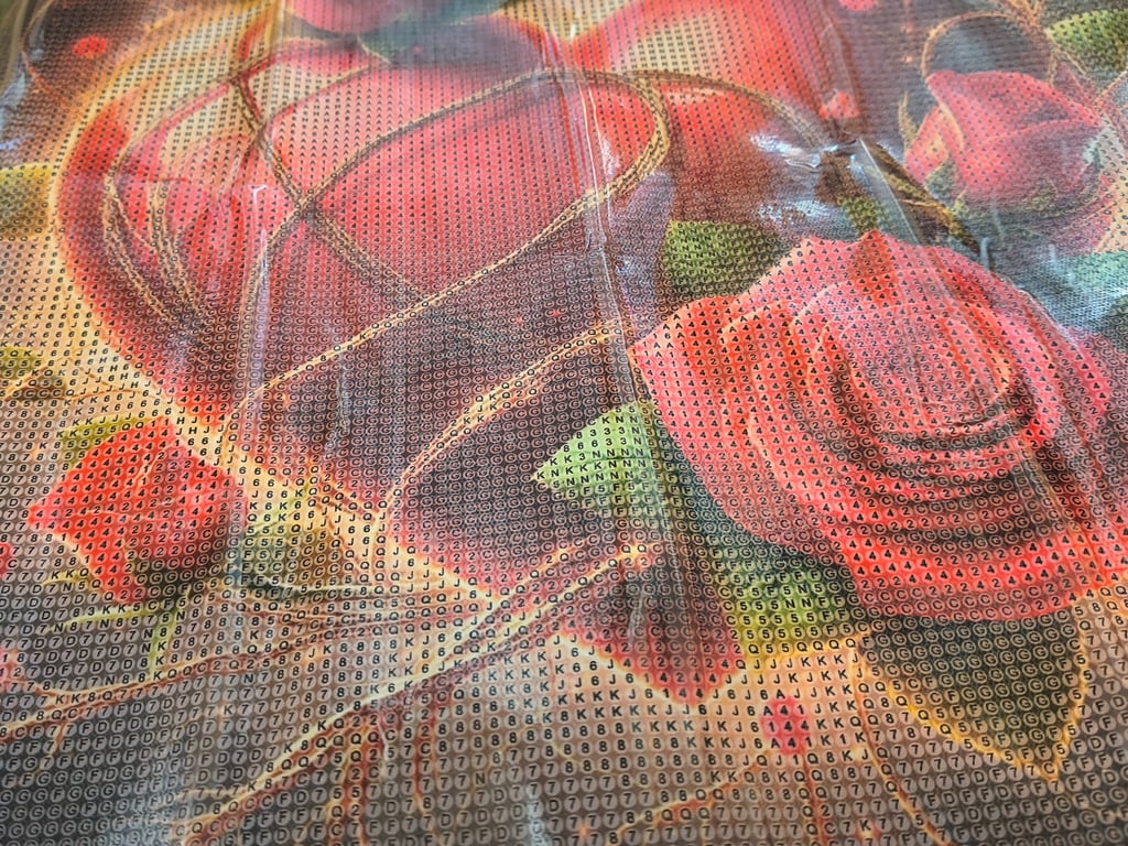 Nærbillede af et diamantmaleri med et blomstermotiv med roser, hvor lærredet har trykte symboler til farvekodning.
