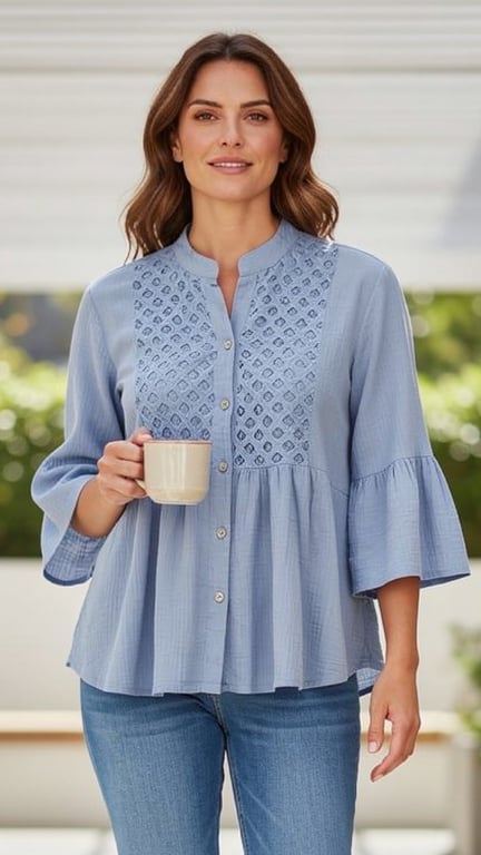 Kvinde iført lyseblå, broderet bluse og jeans, der holder en kop.