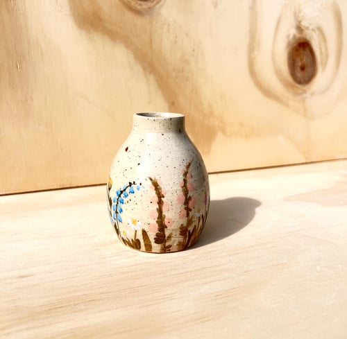 Lille keramisk vase med blomsterdekoration, stående på lyst træbord med lyst træbaggrund. (1)