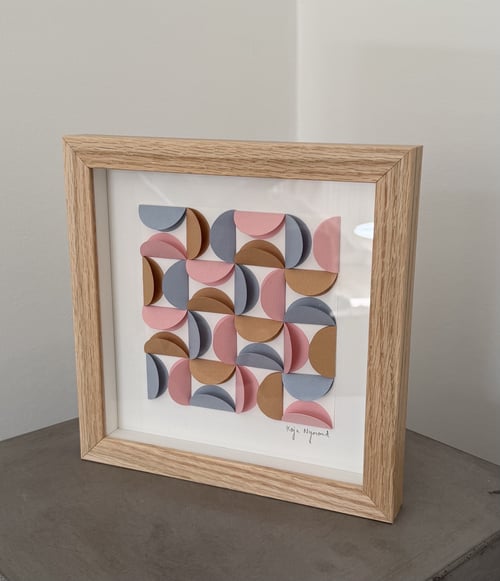 Indrammet abstrakt kunstværk bestående af farvede halvcirkler i blå, rosa og brun, arrangeret i et geometrisk mønster. (1)