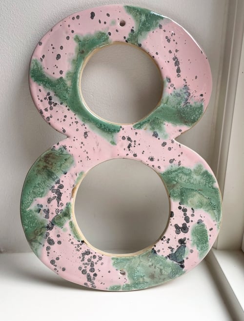 Keramiktal otte med pink, grønne og sorte pletter, placeret på en hvid flade ved et vindue. (2)