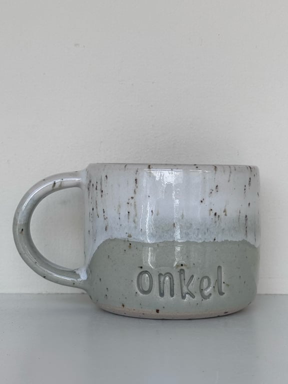 Grå og hvide keramikkrus med teksten "onkel" præget på fronten.