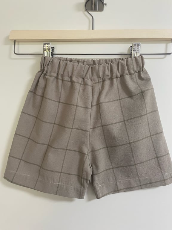 Grå ternede shorts med elastisk talje hængende på en bøjle.