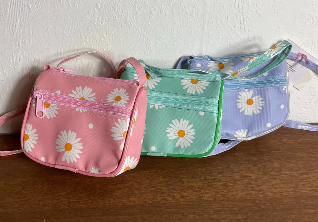 Tre små skuldertasker i pastel pink, mintgrøn og lyselilla med hvidt og orange blomsterprint, placeret på en træflade foran en hvid væg.