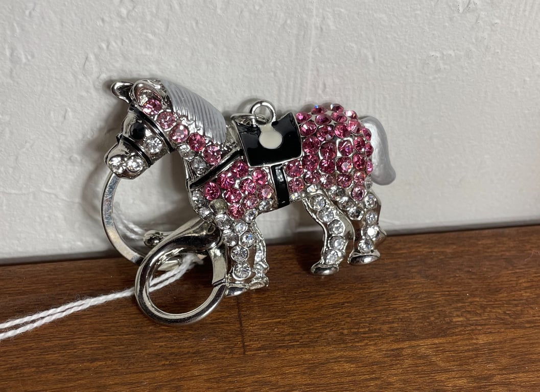 Nøgleholder i form af en pony med rosa og klare krystaller, sat på et brunt bord ved en hvid væg.