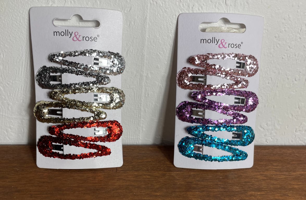 To sæt med glitrende hårspænder i forskellige farver på papkort med mærket "molly & rose", placeret på et brunt bord foran en hvid væg.