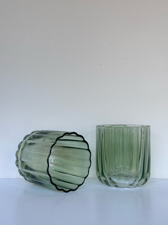 To grønne, rillede glas, hvor det ene står oprejst, og det andet ligger på siden mod en hvid væg.