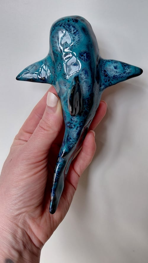 Hånd holder en glaseret keramisk figur af en delfin i blå og grønlige nuancer. (1)