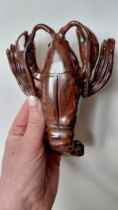 Hånd, der holder en brun glaseret keramisk skulptur formet som en hummer. (1)