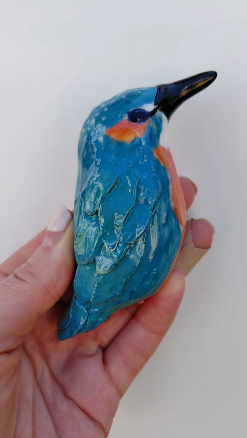 En hånd der holder en lille, glaseret keramisk fuglefigur med blå, orange og sort farver. (1)