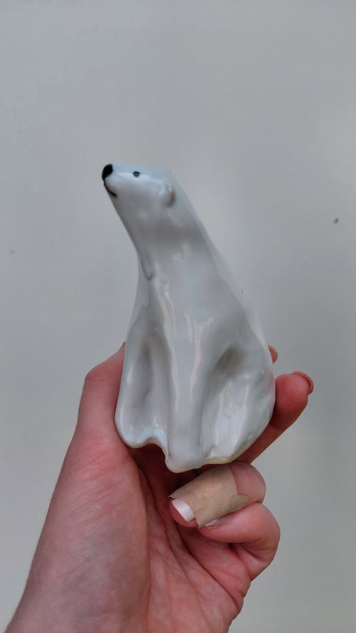 Hånd, der holder en hvid porcelænfigur af en siddende isbjørn. (1)