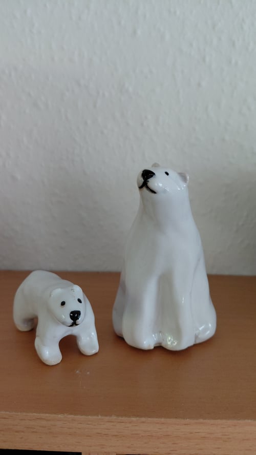 To figurer af hvide isbjørne i porcelæn placeret på en træflade foran en hvid væg. (1)