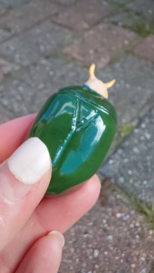 Hånd, der holder en grøn, blankt malet figur formet som en lille okse med gule horn. (1)